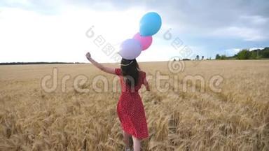 快乐的女孩穿着红色的的快乐女孩手里<strong>拿</strong>着<strong>气球</strong>穿过金色的麦田。 年轻女子棕色